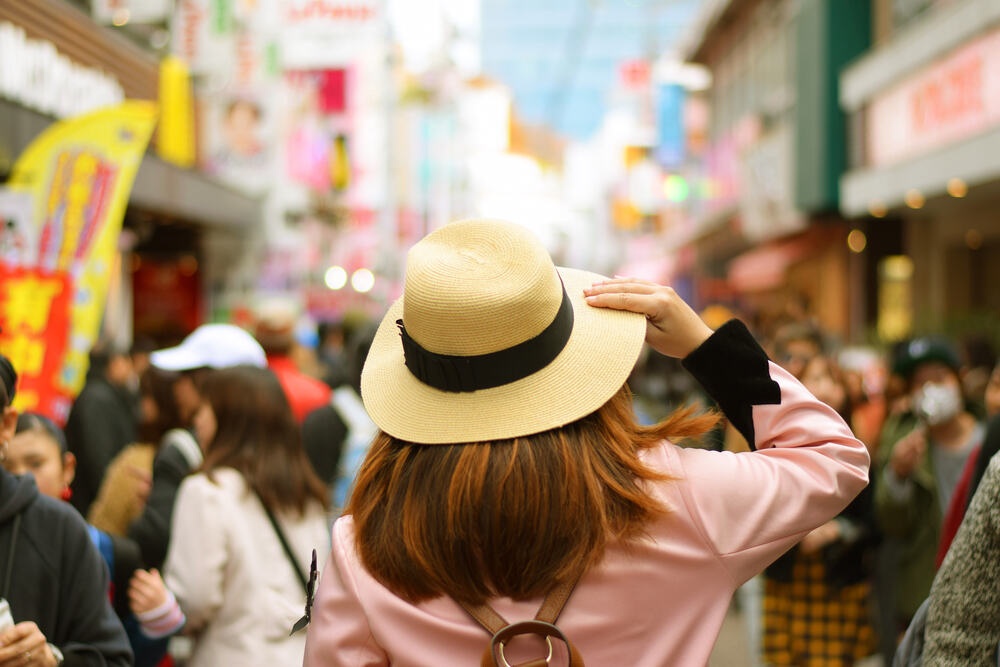 นักท่องเที่ยวหญิงใส่หมวกยืนอยู่ในวิวย่านฮาราจูกุเมืองโตเกียว